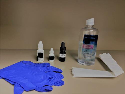 Figure 1 Set up for in-office povidone-iodine irrigation. From left to right: nitrile gloves, topical anesthetic, topical NSAID, betadine, 5% solution, saline solution, and folded paper towel for saline rinse.