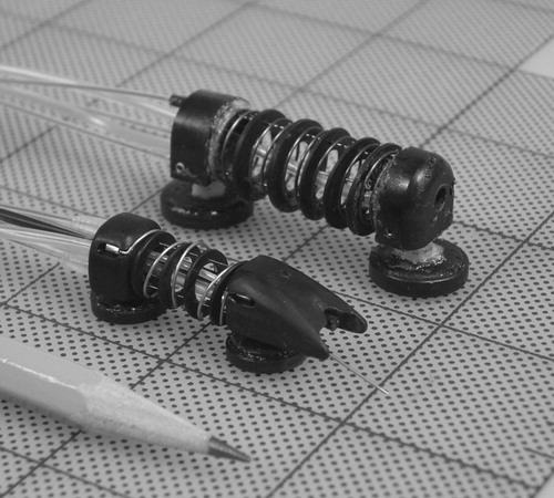 Figure 2. The first crawling robot prototype (upper: 18 mm tall, 14 mm wide) and second prototype (lower: 11 mm tall, 10 mm wide). The second prototype features a needle for myocardial injection, which is retracted during locomotion. The lines mark a 25.4-mm grid, and a standard pencil is included for scale.