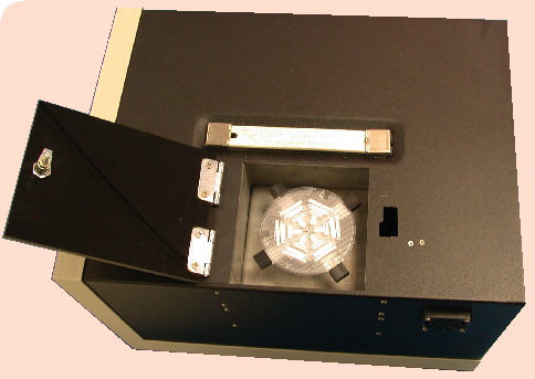Figure 6. Bronx box® for detection of drug resistance.The circular disposable is inoculated in the center slot, and is then sealed for the rest of the process. The sample moves into the first six wells, which contain the appropriate antibiotic or control. Using the centrifuge integrated into the main unit, the sample is then moved to the next ring of six wells, which contain luciferase reporter phage. The phage are given time to infect any living mycobacteria, and the sample is then moved into the next ring of six wells, which contain luciferin. Phages that infect living mycobacteria will produce light, which is detected and analyzed by the main Bronx box unit. Image courtesy of Sequella, Inc. (MD, USA) and reproduced with permission.