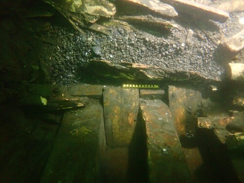 Figure 16. Ballast of flint shingle at the bottom of the ship. This material could have been obtained in various locations along the Atlantic or North Sea coasts. Above the ballast is firewood of freshly cut birch, 0.5–0.7 m long. These are slightly shorter than similar firewood (also birch) found on Mary Rose (1545) and indicate that the galley was proportionally smaller than on the English ship but was in a similar position in the hold (compare Dobbs Citation2009a, Citation2009b). (Photo: Johan Rönnby).