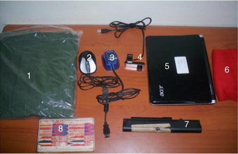 Fig. 2 Computer hardware and logistics: (1) the raincoats; (2) the mouse; (3) the biometric fingerprint devices; (4) the web cameras; (5) the mini-laptops; (6) the red calico used for the background of the photos taken; (7) the spare batteries for the mini-laptops; and (8) the field notebooks used.