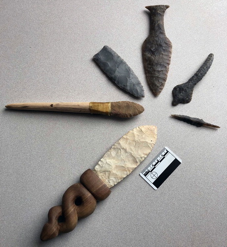Figure 4. Examples of Patten’s flintknapping. Clockwise, starting at the bottom: Burlington chert biface hafted on a black walnut haft carved with an Anatolian design; quartzite Folsom point hafted onto a foreshaft; Clovis point on Georgetown chert; Danish Dagger; Cobra; Danish trihedral point.
