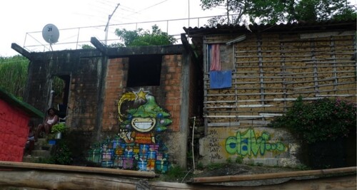 Figure 7. Maria sits in front of her burned-down house marked for eviction next to a painting by local artists for the Christmas celebrations (photo by the author, 2012).