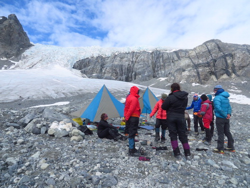 Figure 2. Participants gather for a meal at the kitchen area at base camp on the Gulkana Glacier (C'ulc'ena'Luu’) in Alaska, in front of the active Gabriel Icefall. Participants’ sleeping tents are also in the vicinity, located atop the same exposed band of glacier-eroded cobbles. Photo by lead author.
