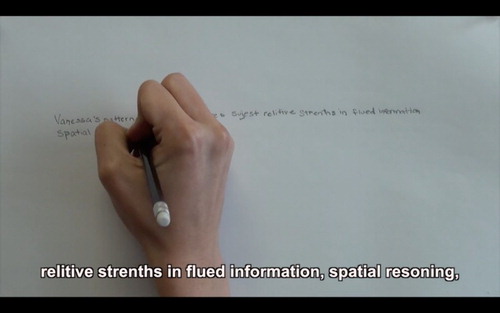 Figure 8. Still frame showing a hand writing out words from a diagnostic report from WORDS by Vanessa Dion Fletcher. A caption reads ‘relitive strenths [sic] in flued information, spatial resoning’.