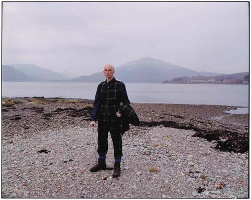 Figure 1. Artist Michael Sanders wearing the Polaris Military tartan suit he designed, standing across the bay from Coulport, north of Holy Loch, where Polaris missiles were housed and maintained during the Cold War. Image ©️ 2017 Michael Sanders. All rights reserved, DACS.