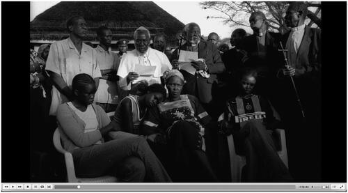 Figure 1 Rebecca and her family while mourning Dr Garang’s death. She is accompanied by clergy, family, and other community members. (Screen freeze-frame from No Simple Way Home). Accessed from Afri Docs’ (@AfriDocs)—https://youtu.be/90m7gpKKnqU