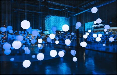 Figure 3. Inside the Estonian pavilion in EXPO 2020. Photo: Mihkel Sillaots. Figure 3 A photograph of room with sphere shaped lamps hanging from the ceiling in different heights, shining with blue light.