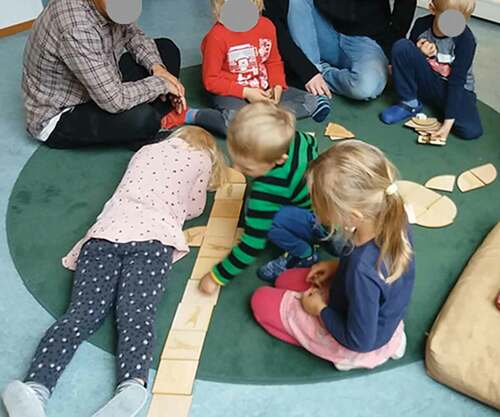 Figure 5. Children playing with the wooden pieces they created in the previous design workshops. In the illustrated situation, the children take the roles of actors, deciding how to play with the pieces. Adults are whisperers and supporting the actions, but allowing the children to act on their initiative.