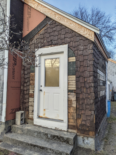 Figure 5. A view of the side vestibule after asphalt shingle siding had been partially stripped, revealing original window shapes boarded over, and original 1886 cedar shingle details. Photograph by Kris Manjapra.