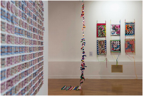 Figure 16 Installation view with background in focus of Migrations, Huddersfield Gallery of Art, England (October 22, 2016 - January 21, 2017). Left: Claire Barber You Are the Journey (An Embroidered Intervention) (2015), used ferry tickets, reclaimed yarn, pins, and needle weaving over used ferry tickets (detail); middle: Françoise Dupré, Stripes, started in 2009 in Mostar, Bosnia-Herzegovina with straps of bags used in OUVRAGE project - 2011 woven webbing, straps from carrier bags and thread, bamboo cane, and hooks; right: Françoise Dupré, Arabesques, Stars with Dragon (2014), wall hanging installation, stitched woven and printed polythene, polyester/cotton bias, thread, quilting pins, acrylic knitted flat braids, and six stainless steel screw rings.