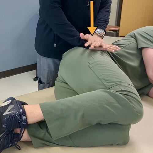 Figure 5 Compression Test – The patient is positioned in a lateral decubitus position, facing away from The Examiner, and their painful SIJ facing away from the table. While standing at the level of the pelvis, The Examiner applies a firm downward force through the ilium as seen by the arrow.