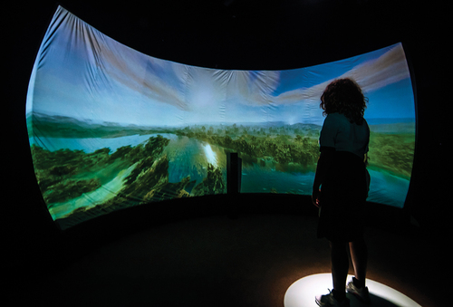 Figure 2. I-ME guides the visitor to the next room with a large curved screen, and says ‘Child of Now lives on the Birrarung, the river of mists that has sustained and been sustained by the Wurundjeri and Boonwurrung people for so long it may as well be forever. Ten thousand years ago the river ran through a fertile plain to the sea.’ on screen, the 8-minute animation of 10,000 years of life on Birrarung river begins with the flooding of Naarm (Port Phillip Bay, Melbourne).