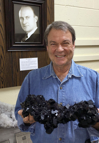 Ed Clement holding a fluorite specimen from the Illinois-Kentucky fluorspar district and standing in front of a photo of his father, Ed Clement Sr.