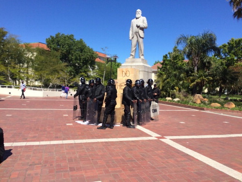 Figure 2. Flight, Nicolene Burger. Photograph by Open Forum Collective, Stellenbosch University, 2016. The armed, private security firm that students refer to as the ‘Men in Black’ surround the sculpture a few minutes after it was installed on the Rooiplein. Their apparent deployment here was to protect the sculpture of Jan Marais.
