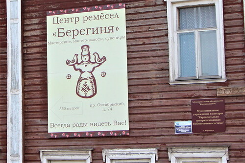 Figure 7. A large two-color poster with the title of the “Bereginya” folk craft centre, an image of Bereginya toy with two birds in her hands raised up to the sky, the address of the Centre, and a welcoming phrase underneath. The poster is hanging on a wall of a wooden building in the city centre. Photo by V. Kobyshcha.