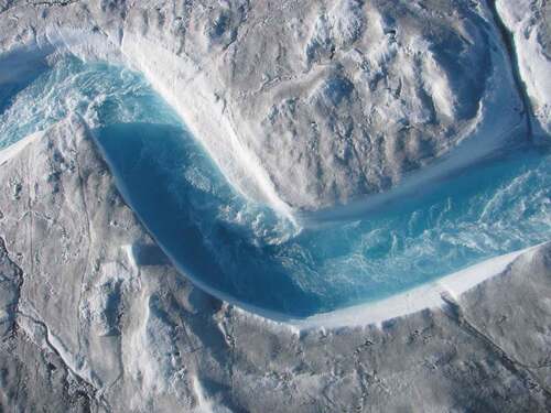 FIGURE 9 A supraglacial meltwater river flowing across the surface of the southwestern Greenland ice sheet. Ocean-going flows from hundreds of supraglacial rivers in this area are a key mechanism by which climate change is rapidly rising global sea levels, imperiling the world’s coasts (Smith Citation2020). [Well-being] (Author photo from helicopter, 2012).