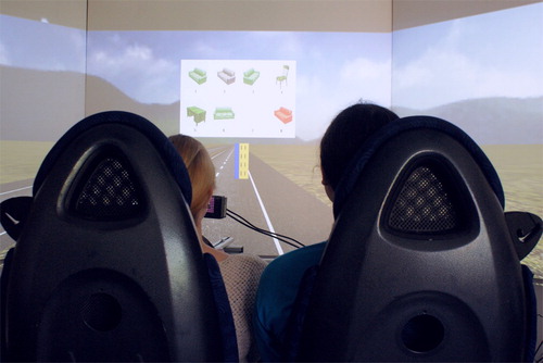 Figure 2. The driving simulator used for this experiment. Speaker-passengers described a target image from the image array displayed above the road. Listener-drivers had to follow the yellow bar back and forth across the road while identifying the intended referent by number.