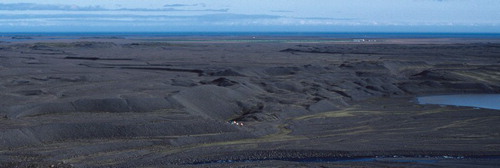 Figure 4. View southeastwards across the outwash head at Heinabergsjökull, showing (in the distance) the expansive, terraced surfaces of the proglacial outwash fans grading to the coast and (in the middle distance) the staircases of pitted kame terraces and associated push moraines on the ice-contact face. The tents lie in a large melt-out hollow that abruptly terminates one of the kame terraces feeding in from the left and which demarcates the extent of glacier ice previously buried by glacifluvial terrace sediment. The terraced alluvium that feeds into the modern lake delta is visible in the foreground, with the modern lake on the right.