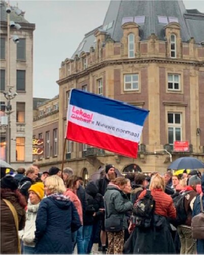 Figure 2. Protestors carry an inverted Dutch flag, symbolising the state of emergency that they consider the Netherlands to be in, that reads ‘Global Local = The New Normal’. Photographed by first author at the Dam square in Amsterdam, 6 November 2022.