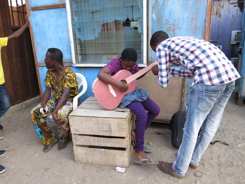 Figure 3. Guitarist Stanley Dzane (aged 24) teaches Daniela on the glittery pink guitar. They are among members of the Line Out Family Band. Bandleader Nana, who bought Daniela’s guitar, is on the left.Photo by the author © Katharina Gartner 2015 in Accra, Ghana. Reuse not permitted.