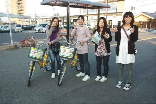 Figure 2. Young female visitors traveling around Shiroishi city using rental bicycles (in front of JR Shiroishi Station).(Source: Photograph courtesy of Shiroishi City General Affairs Department, Planning and Information Section, October 2010.)