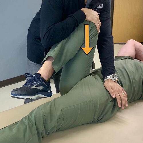 Figure 2 Thigh Thrust Test (Posterior Shear Test) – With the patient lying in a supine position the hip and knee ipsilateral to the painful SIJ are flexed, and the femur is positioned perpendicular to the table. A linear downward force through the femur towards the table is applied as depicted by the arrow.