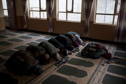 Taliban members lay their weapons down as they pray inside a mosque in Kabul, Afghanistan, September 2021. Courtesy of AP Photo / Felipe Dana / Alamy