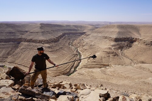 Figure 1. The author documenting the massive tower structure with the wadi in the background. Image courtesy of the author.