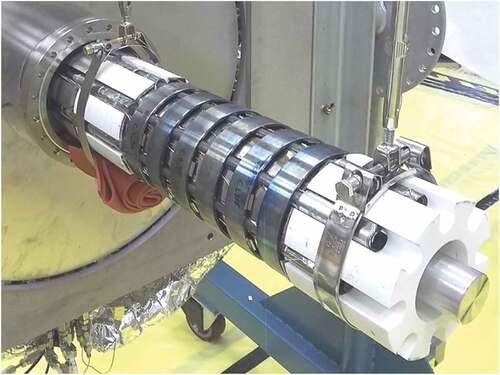 Fig. 2. The assembled KRUSTY reactor core ready to be enclosed within the vacuum vessel. Six Haynes 230 rings are clamping the Na heat pipes to the HEU UMo core, with white BeO axial reflectors on both ends. A temporary fixture to aid assembly (soon to be removed) protrudes from the bottom and surrounds each reflector. The vacuum flange is on the far left.