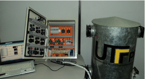 Figure 3. Picture of the laboratory testbed used in the experiments. Notes: The apparatus comprises the grain silo prototype that stored wheat infested by R. dominica, the electrical control panel that implemented the control of temperature inside the silo, and a computer that collected and saved all of the data corresponding to the experiments.