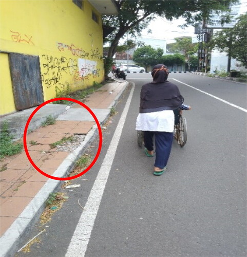 Photo 5. A photo of Participant 1 on a wheelchair and his carer. Participant 1 prefered to go through the road with his wheelchair, because the sidewalk was in poor condition, with cracks and grass growing on it.