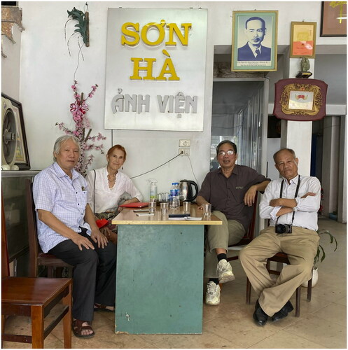 Figure 1 A photograph of Khánh Ký, regarded as the first teacher of the Lai Xá photography craft, has a place of honor on the wall of Studio Sơn Hà. Left to right: Nguyễn Văn Huy, Laurel Kendall, studio proprietor Nguyễn Minh Nhật, and Lai Xá Photography Museum director Nguyễn Văn Thắng. (Photo by Bùi Thu Hoà)