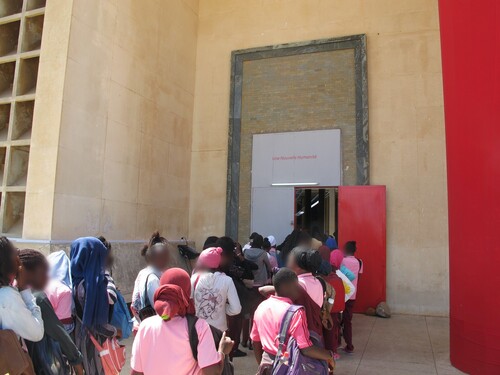 Figure 1. School groups waiting to enter at the main entrance to the Palais de Justice, the central venue of the 2018 Dak’Art. The theme was “L’Heure Rouge,” and the door and columns had been painted crimson red; above the door, newly posted in red lettering, it read “Une Nouvelle Humanité,” all references artistic director Simon Njami had drawn from the writer Aimé Cèsaire. Photograph by author.