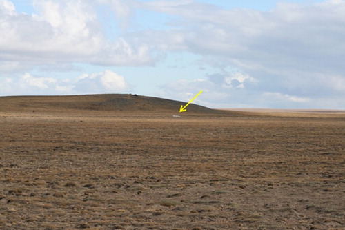 Figure 9. Scoria cone overrun by glaciers and degraded by cryogenic processes. A huge erratic boulder at the slope foot is pointed out by the arrow.