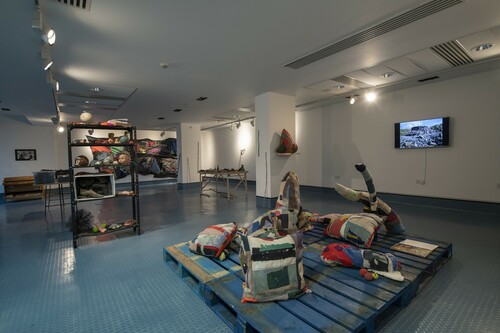 Figure 7. Sally Madge: Acts of Reclamation, © Amy Madge and Lucy Madge, Photo: Colin Davison.The Scatter cushions as displayed on a series of distinctive blue pallets, an equal and complementary bridge between the dominant gallery floor and the objects on display.