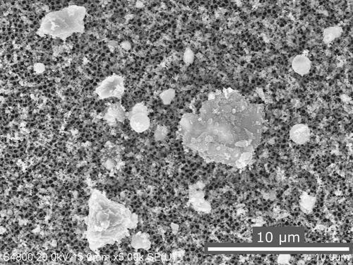 Figure 11. SEM image of NMC cell explosion aerosols collected on an anodisc membrane with a 5-sec sampling time. The black pores of the anodisc membrane are visible below the collected aerosols.