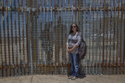 Figure 4. Griselda San Martin, The Wall, 2015–16. Family portrait. Rosario Vargas (in the foreground) with her daughter Jannet Castañon and grandson Hector, 15, (behind the border wall, on the U.S. side.) Rosario and her daughter live just a few miles apart but have been separated by the U.S-Mexico border wall for almost 10 years. On April 30, 2016, they were one of the few families who were allowed to briefly reunite for 3 min when a small door in the fence was opened. But once the door of hope was closed, the reality of the border hit them again. They see each other every weekend through the metallic fence. Photograph © Griselda San Martin.