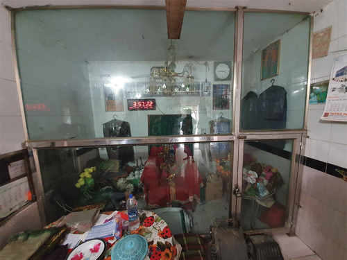 Image 3. The memorial premise; the chair covered by a red cloth and placed at the center. some chairs, some of his old cloths, a couple of prayer mats, few tea cups, a couple of watches, flowers made by plastics, and a picture of Haidar Baba.Photo Credit: Ethnographer