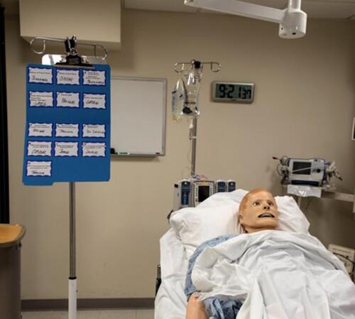 Figure 1 Photograph of a mock simulation laboratory using the Orchestra Leader’s chart, with roles displayed, mounted on an IV pole at the head of the manikin and clearly visible to the entire group.