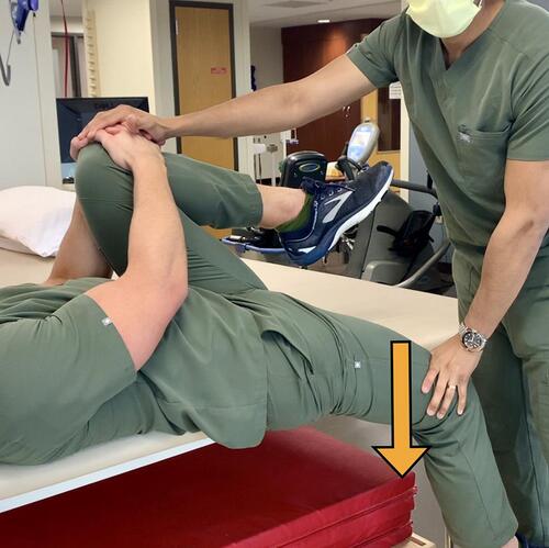 Figure 3 Gaenslen Test – While stabilizing a patient’s flexed knee, a counter force depicted by the arrow is applied through the hanging leg towards the floor.