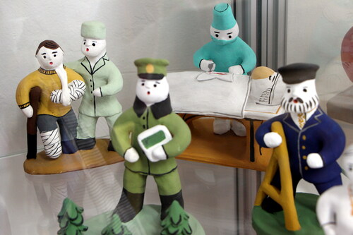 Figure 4. Bespoke clay toys representing a surgent operating on a patient, a nurse helping a patient with broken arm and leg, and a border guard in the forest of pine trees. Created by the crafswomen of the Center for Folk Crafts “Bereginya.” Photo by V. Kobyshcha.
