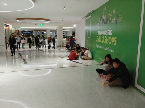 Figure 10. In a shopping mall food court while the seating area remains closed, people sit on the floor to have their food there anyway.