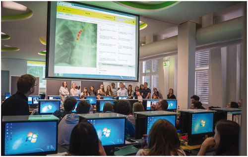 Figure 2. Small groups of about 18 students, supervised by a radiologist, discuss the individual work. The big screen presents the ‘PRISMA’ learning dashboard to the small group in the foreground. In the background is another small group with a radiologist looking at their own learning dashboard.